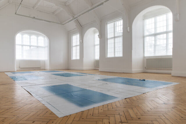 White Gallery space with large white installation on the floor with blue rectangular colourings