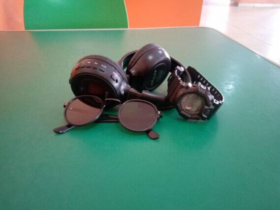A pair of glasses, a watch and headphones placed on a green table.