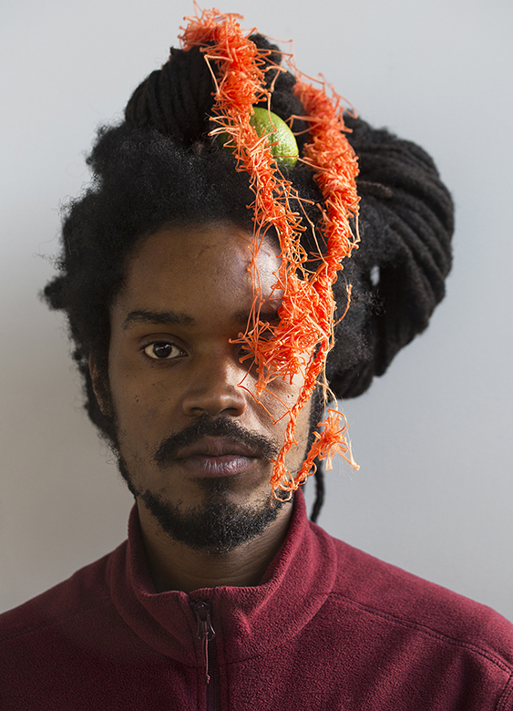 Man against background with orange material over his head and face.
