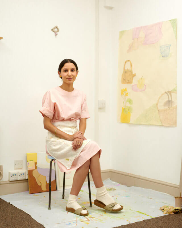 A woman in pastel clothing sitting in an artists' studio.