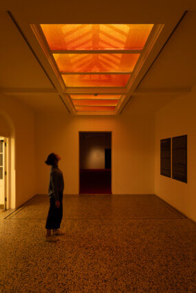 An exhibition visitor looks upwards at the amber skylight installation.
